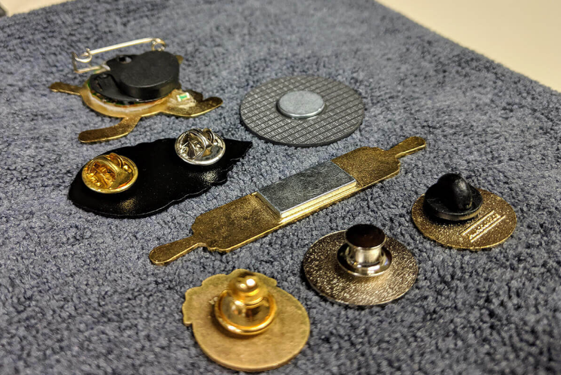 Close-up comparison of enamel pin backing types including butterfly clutch, rubber clutch and locking pin back